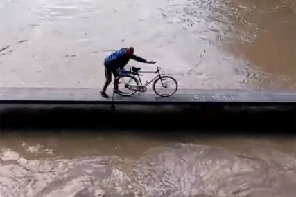 OPASNO I RIZIČNO Čovjek zaštitnim zidom prevezao bicklo pokraj nabujale rijeke (VIDEO)