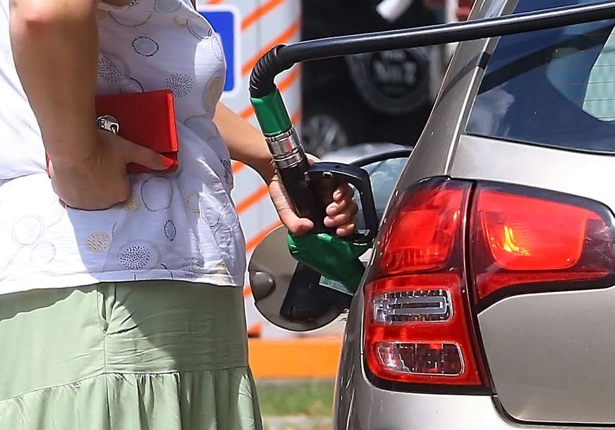 žena stoji pored auta u koji se sipa gorivo