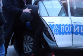 Policajac stavlja uhapšenog u policijski automobil