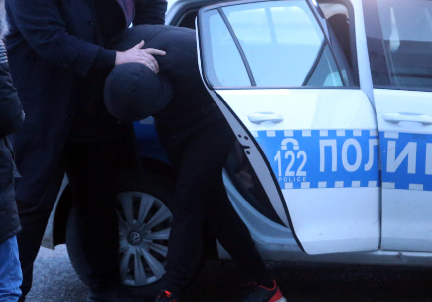 Policajac stavlja uhapšenog u policijski automobil