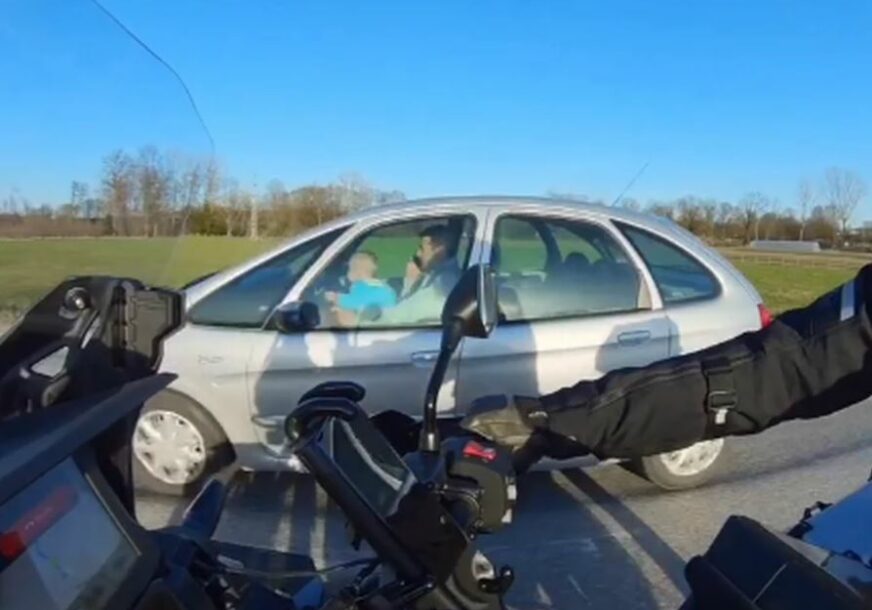 Muškarac priča na telefon i drži djete u krilu dok vozi