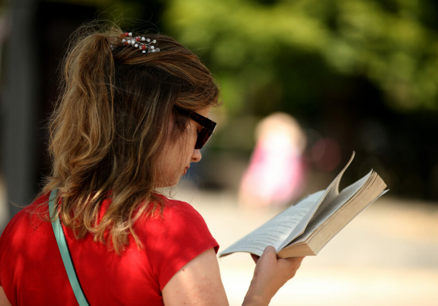 djevojka čita knjigu dok čeka na pješačkom prelazu 
