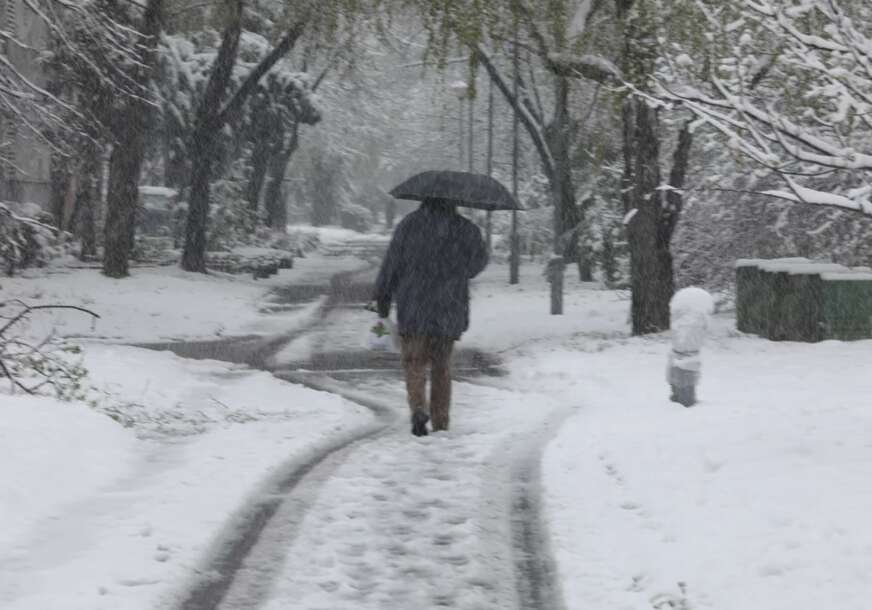 pješak sa kišobranom hoda po snijegu