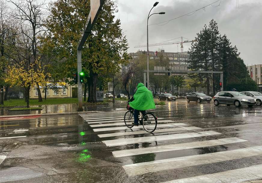 čovjek vozi bicikl i nosi kabanicu