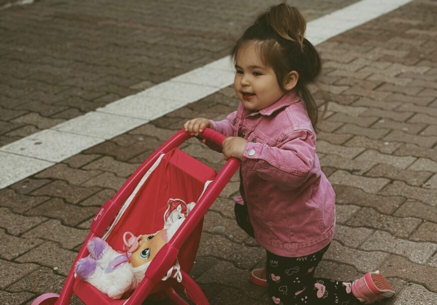 djevojčica vozi dječija kolica za bebu